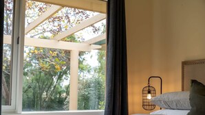 A bedroom with a bed, a window with a view of trees, and a wall-mounted light fixture. - Sandhurst - Stunning Retreat - Pool & Tennis Court (Orange)