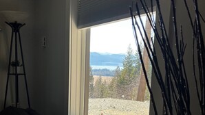 A room with a bed, a window with a view of a landscape, and a tall plant beside the window. - HOT TUB'n at Shuswap Lake
RnR with MnM in our Pet-Friendly! Lakeview Home (Anglemont)