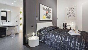A modern bedroom with a large bed, a bedside table with a lamp, a chair, and artwork on the wall. - Minimal flat - Prati, Rome (Roma)