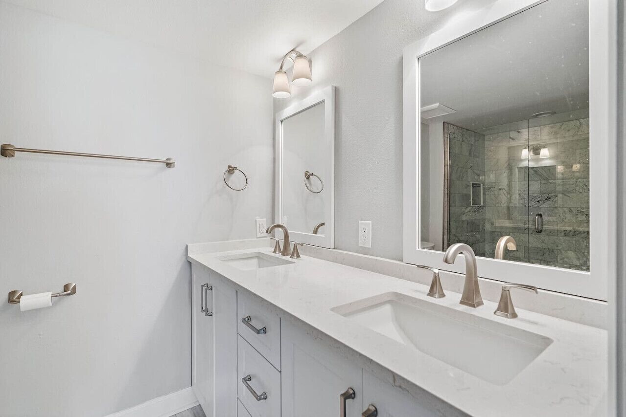 Un baño moderno con dos lavamanos, un espejo grande y una cabina de ducha con mampara de vidrio.