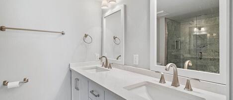 Un baño moderno con dos lavamanos, un espejo grande y una cabina de ducha con mampara de vidrio.
