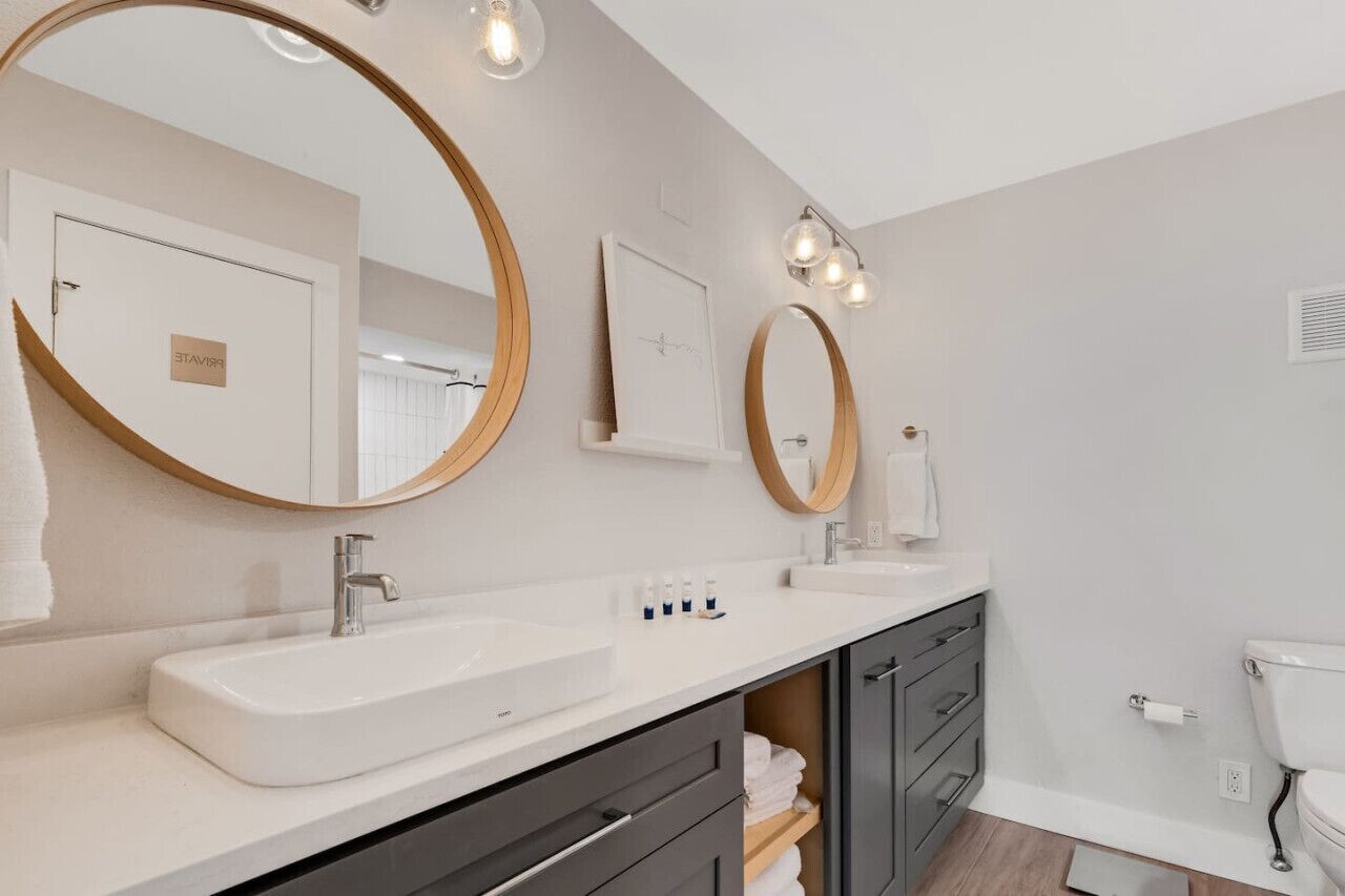 Un baño moderno con dos lavamanos, espejos amplios y un inodoro.