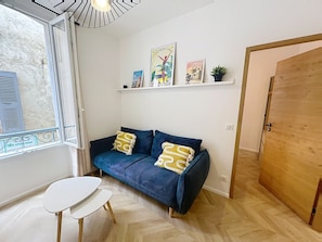 A room with a blue sofa, a small white table, a wooden door, and a window with shutters. - Cannes Meynadier Croisette, Palais Vieux Port 1 mn . 2 BR Olam Properties (Cannes)