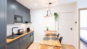 Cozinha moderna com armários cinza, bancada de madeira e forno embutido. Há uma mesa de jantar com quatro cadeiras pretas e um pendente sobre ela.
