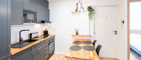 A modern kitchen with grey cabinets, a wooden countertop, and a built-in oven. There is a dining table with four black chairs and a hanging light fixture above.