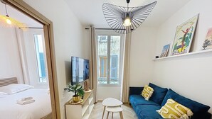 Quarto moderno com cama, sofá, televisão, mesa pequena e planta em vaso.