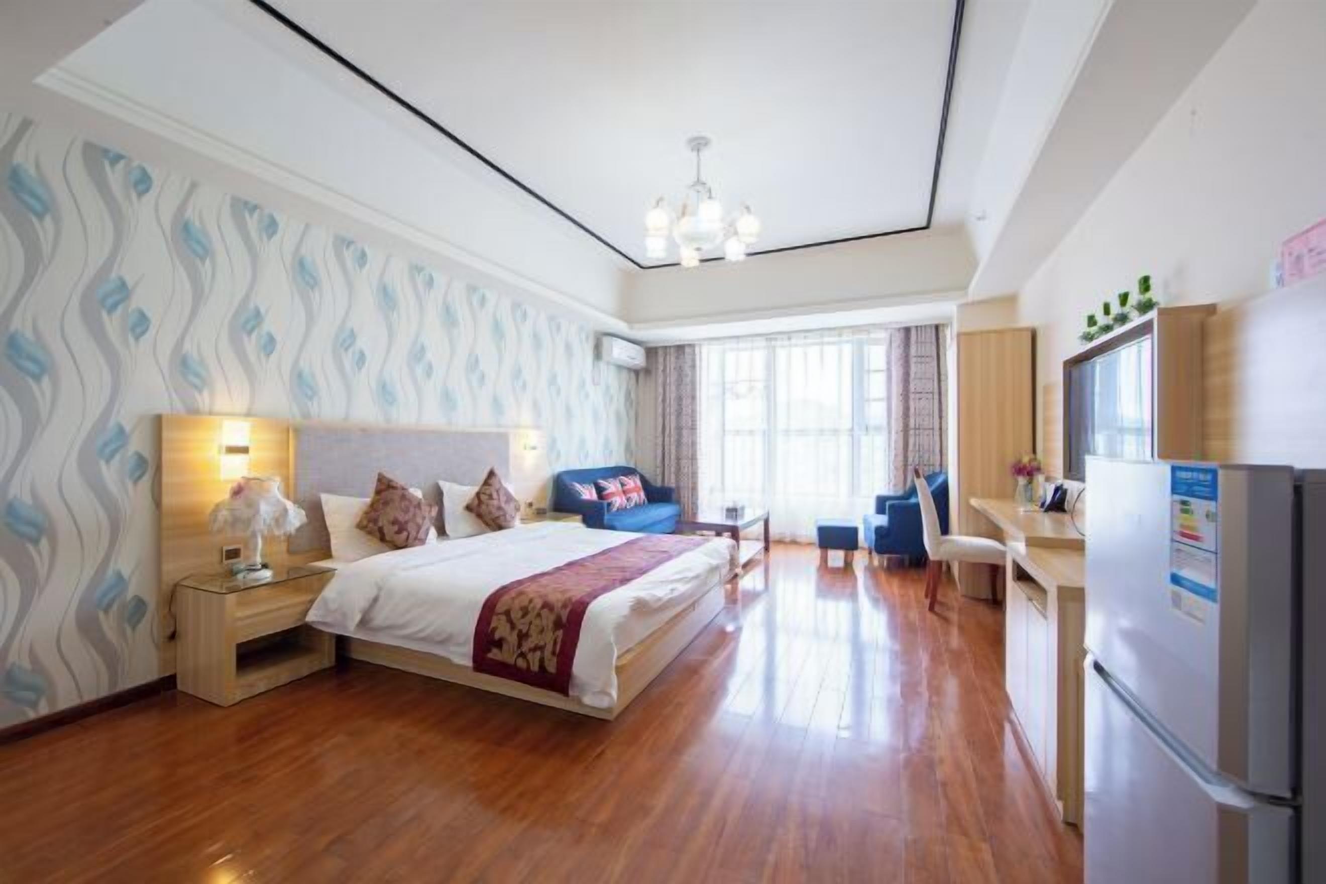 A hotel room with a large bed, a desk, a chair, a refrigerator, and a window with curtains.