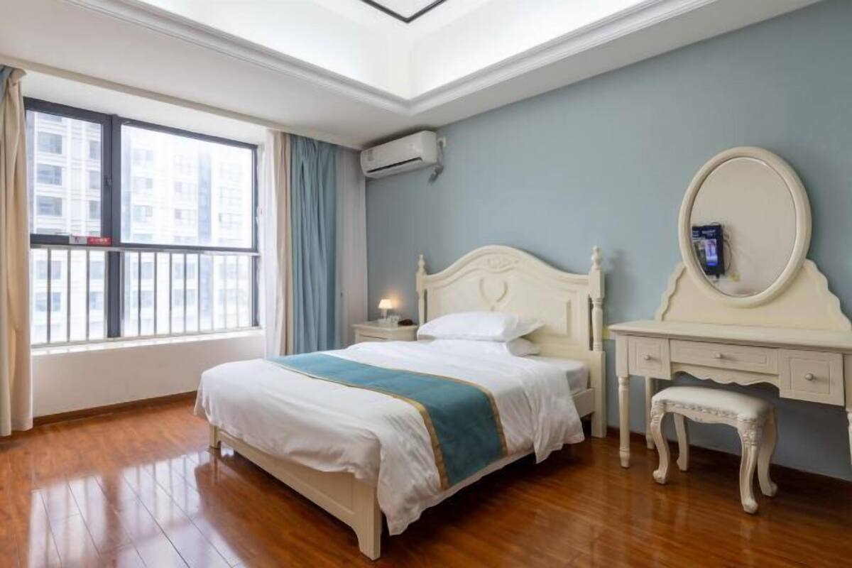 Ein Schlafzimmer mit Bett, Kommode, Spiegel und einem Fenster mit Vorhängen.