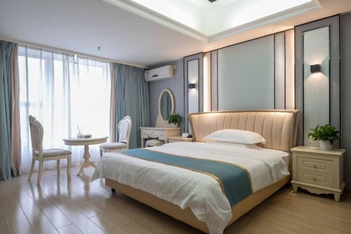 Ein Hotelzimmer mit einem großen Bett, einem Nachttisch, einem Sessel, einem kleinen Tisch und einem Spiegel.