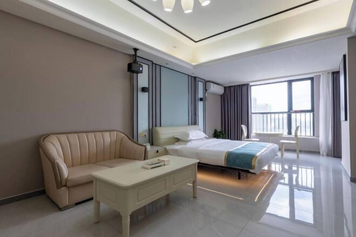 Ein modernes Hotelzimmer mit einem Bett, einer Couch, einem Couchtisch und einem großen Fenster.