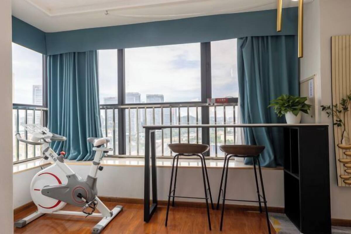 Ein Zimmer mit Blick auf die Stadt, ein Laufband, zwei Hocker, ein Tisch und ein Blumentopf.