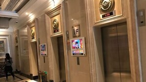 Un espace d’ascenseur doté d’un écran numérique, d’un panneau indiquant le premier étage et d’une personne qui marche au loin.