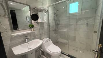 Un baño moderno con ducha de vidrio, un lavamanos blanco y un inodoro.