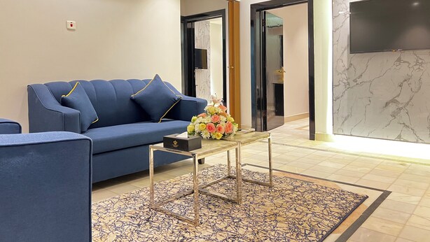A modern living room with a blue sofa, a glass coffee table, and a floral centerpiece. - golden comfort (Hafr Al Batin)