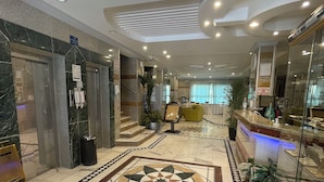 A hotel lobby with marble flooring, a central geometric tile design, a reception desk, and a staircase leading to an upper level. - golden comfort (Hafr Al Batin)