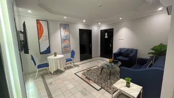 A modern living room with a glass partition, a round coffee table, a blue sofa, and a small side table with a plant.