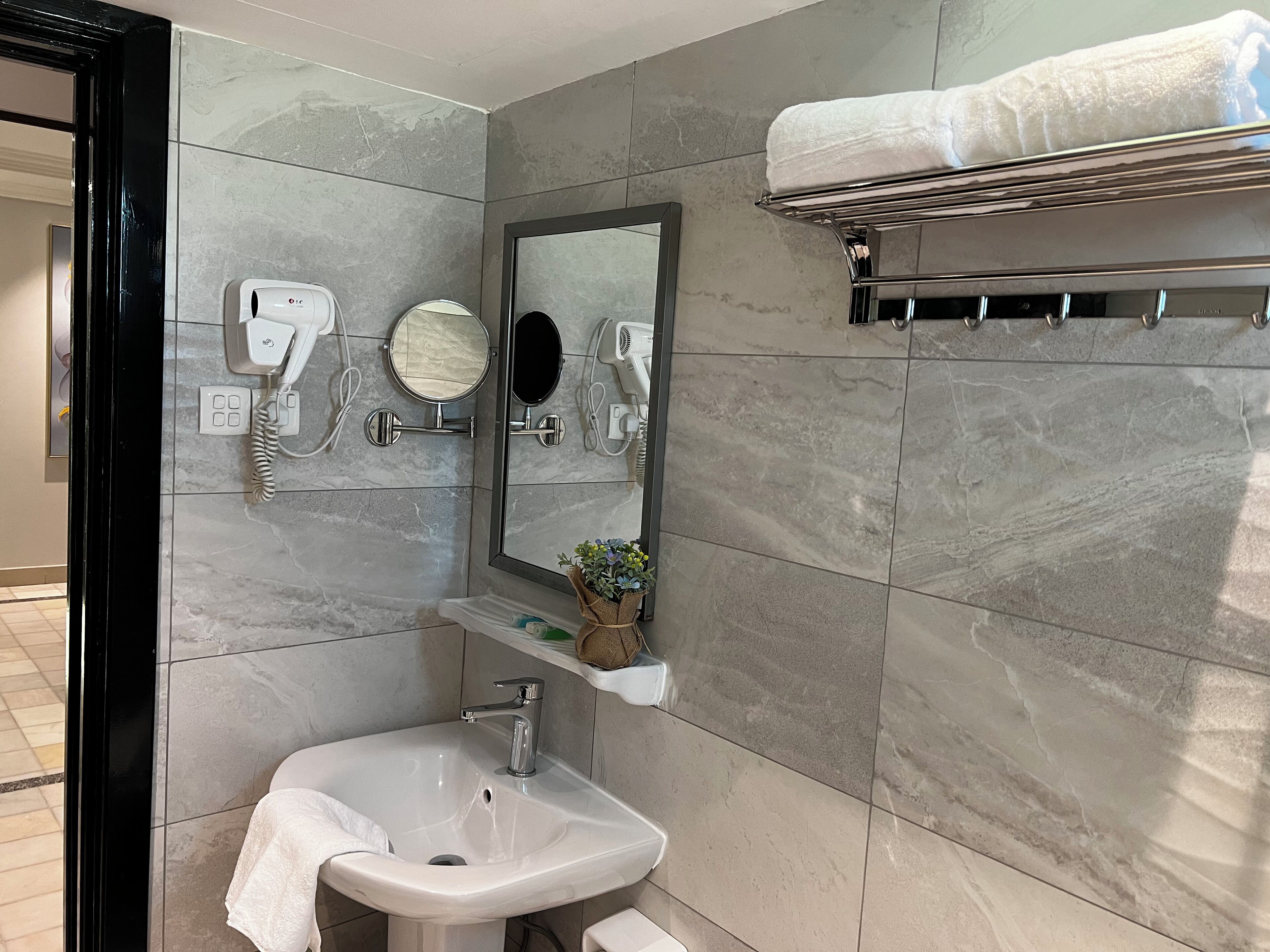 Un baño con lavamanos, espejo, toallero y dos secadores de pelo fijados a la pared.