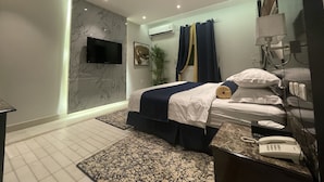 A modern hotel room with a bed, a bedside table with a phone, a TV mounted on the wall, and an air conditioning unit. - golden comfort (Hafr Al Batin)