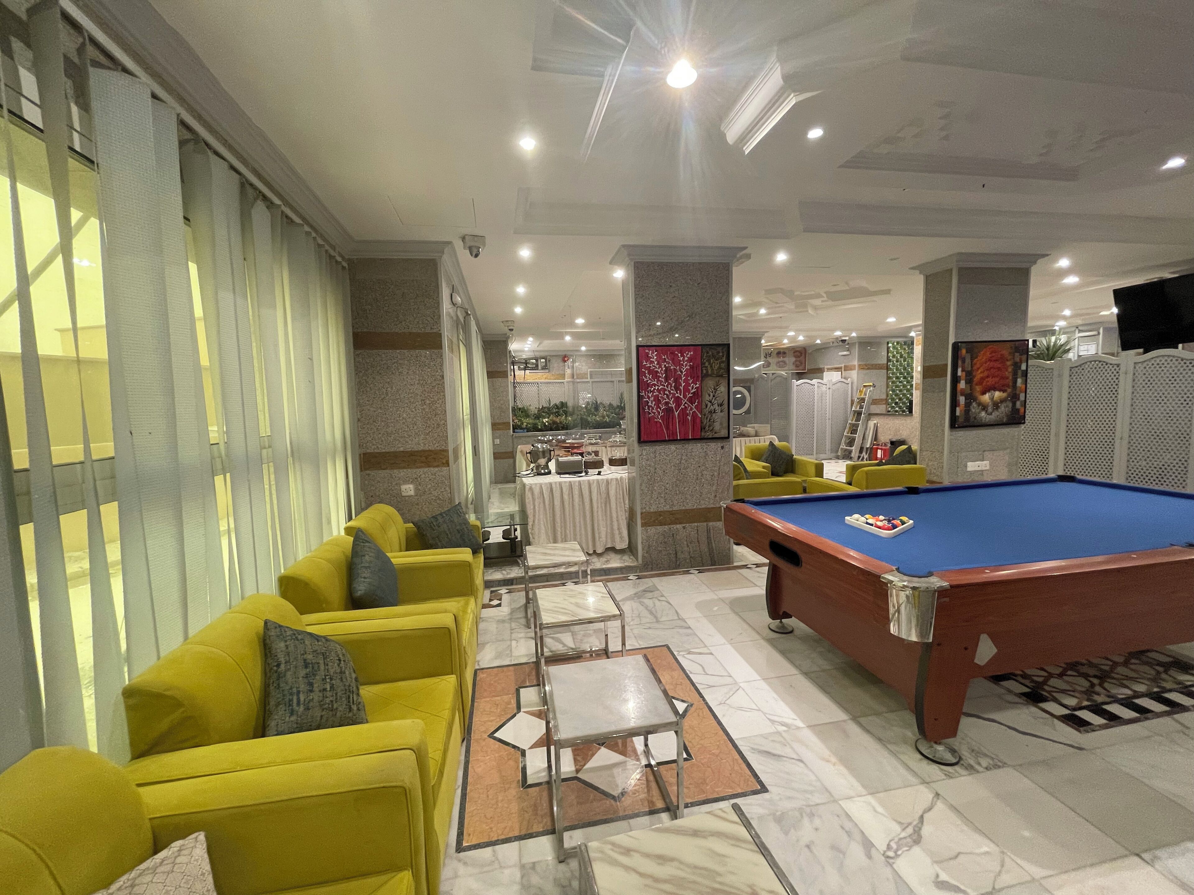 A pool table in a well-lit room with yellow sofas and a marble floor.