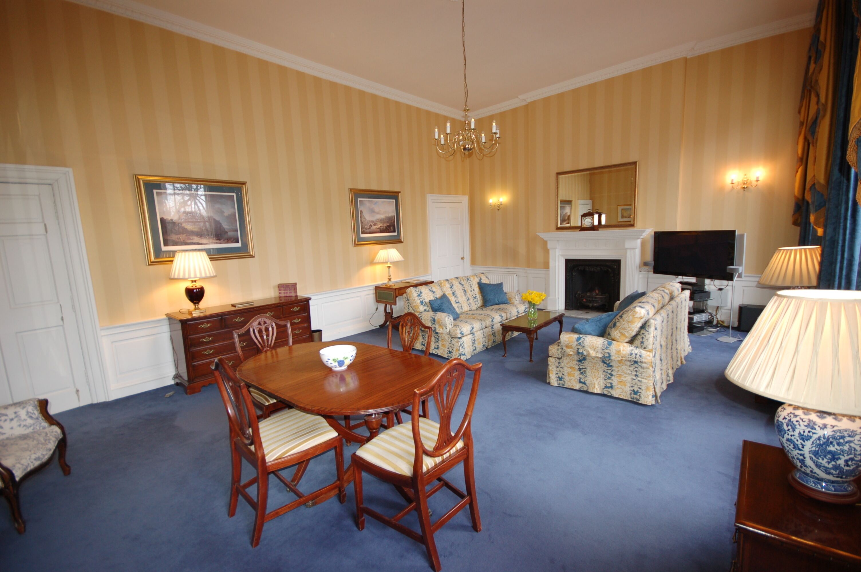 A room with a dining table, chairs, a sofa, a television, and a fireplace.