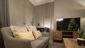 Un salon avec un canapé gris, une table basse en bois et un téléviseur posé sur un meuble en bois.