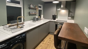 Une cuisine compacte équipée d’un lave-linge, d’une table à manger en bois et de luminaires suspendus.