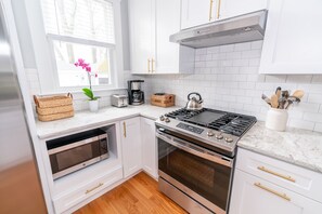 A modern kitchen with white cabinetry, a built-in microwave, a stove, and a coffee maker.