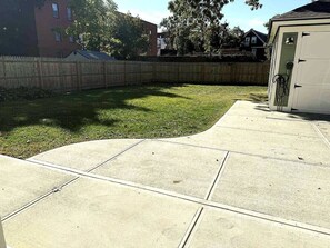 A concrete patio area with a wooden fence and a building in the background. - Edgewood: Close to Yale, Hospital & Park (New Haven)