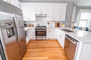 A modern kitchen with white cabinets, stainless steel appliances, and a wooden floor.