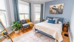 A bedroom with a bed, a chair, a plant, and a painting on the wall. - Edgewood: Close to Yale, Hospital & Park (New Haven)