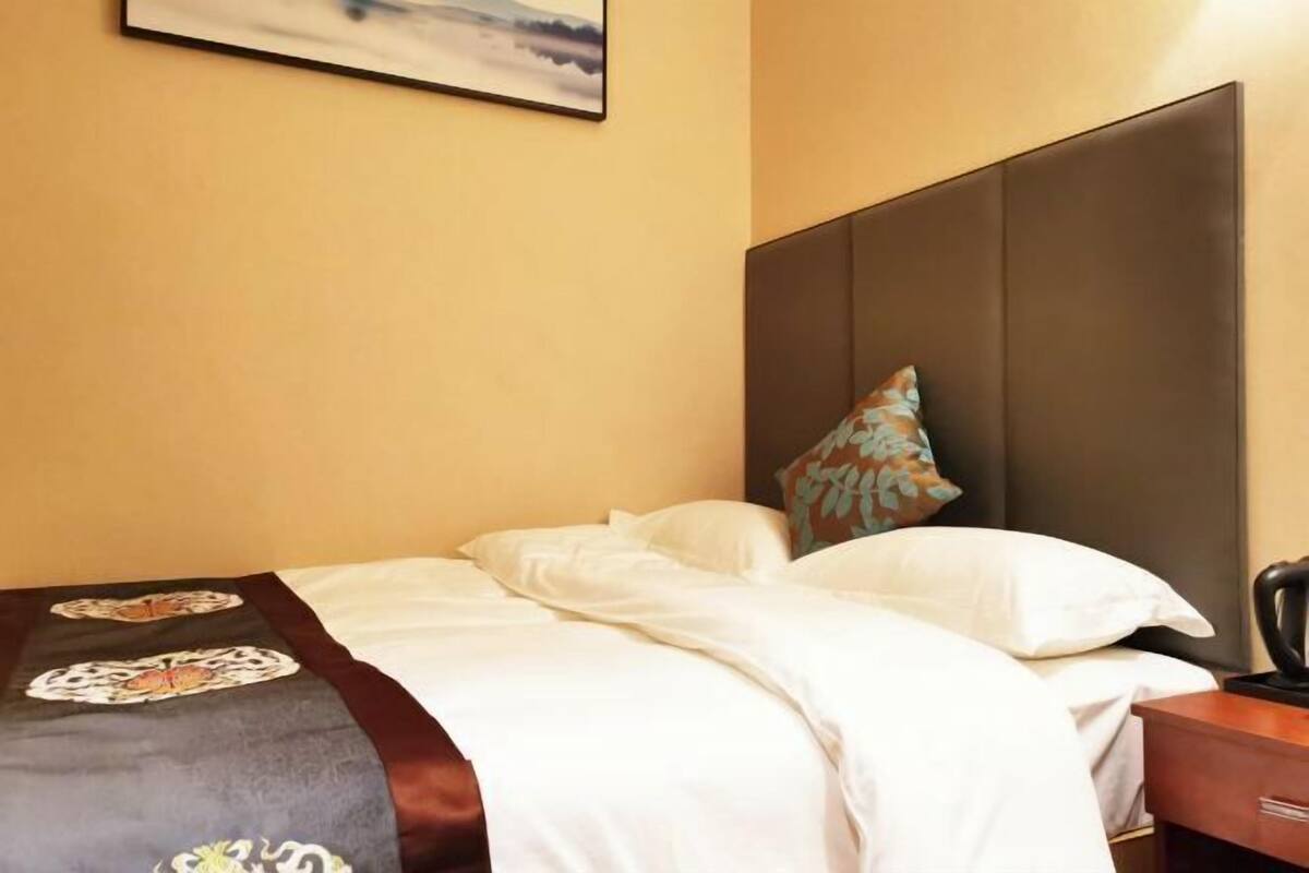 A hotel room with a bed, a nightstand, a lamp, and a painting on the wall.