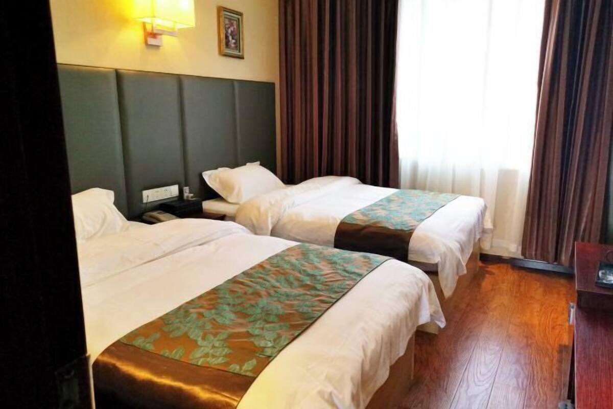 A hotel room with two beds, a nightstand, a lamp, and a window with curtains.