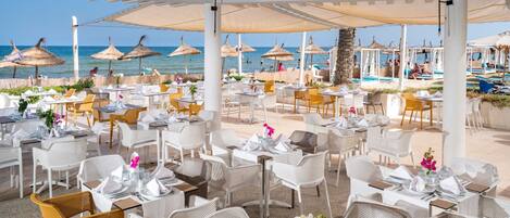 Un espace extérieur aménagé pour les repas, avec des tables, des chaises, des parasols et une vue sur la plage et la piscine.