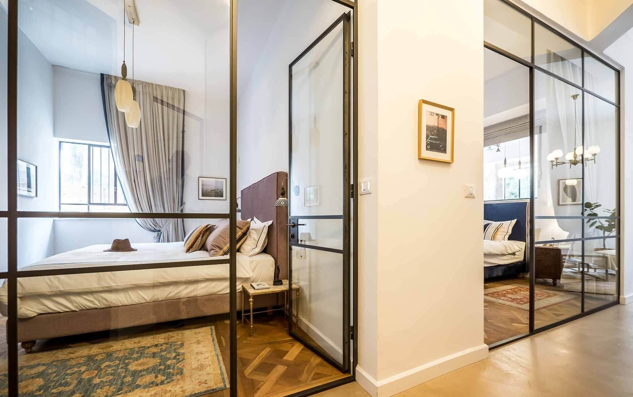 A modern bedroom with a large bed, a nightstand, and a glass partition.