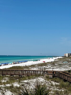 A beach with a wooden boardwalk, beach umbrellas, and a clear blue sky.