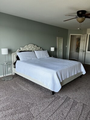 Een opgemaakt bed met een witte deken, een gestoffeerd hoofdeinde en twee bedlampjes.