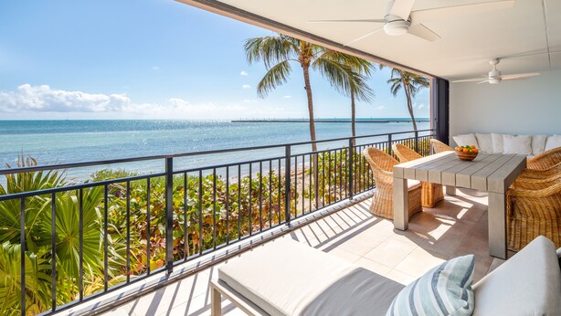 Un balcon avec vue sur l’océan, des meubles en osier et un ventilateur de plafond.
