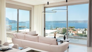 Una sala de estar moderna con un sofá grande, una mesa de comedor y vistas a una ciudad costera a través de ventanales.