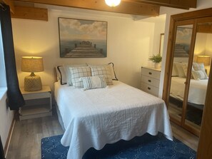 Une chambre à coucher comprenant un lit, une table de chevet, une lampe, une commode, un miroir et un tableau représentant une jetée.