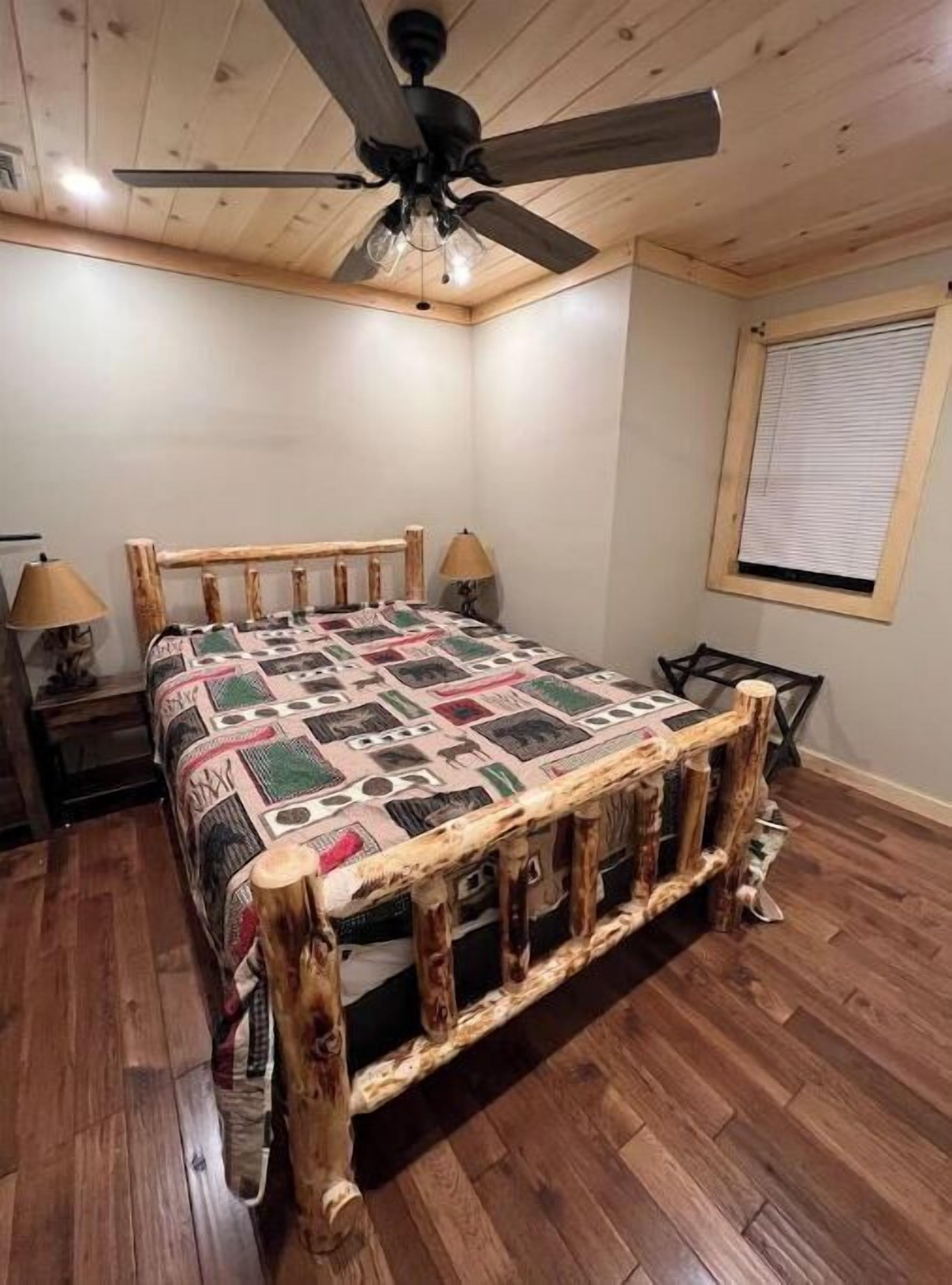 Un dormitorio con estructura de cama de madera, ventilador de techo, ventana con persianas y piso de madera.