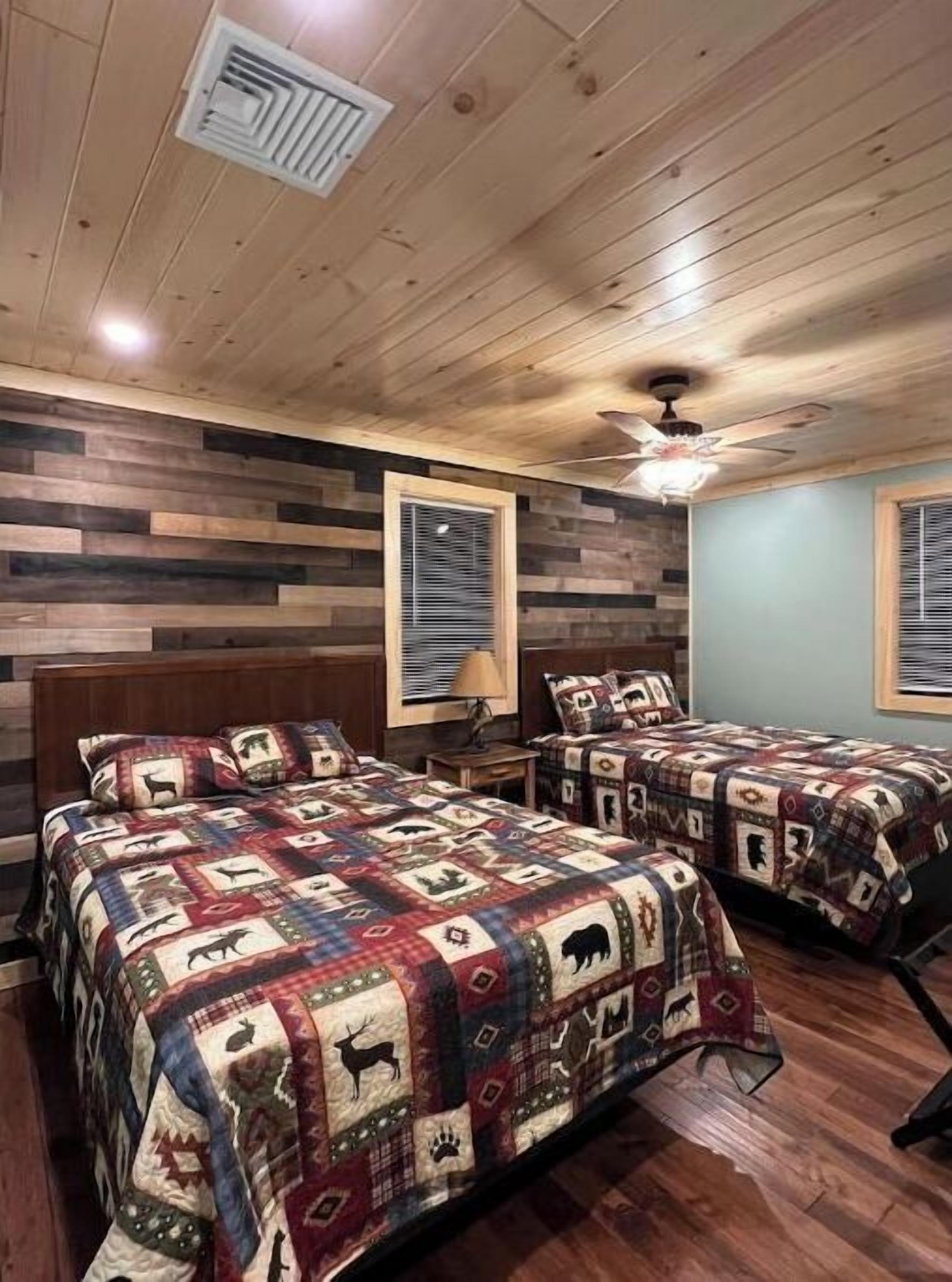 A bedroom with two beds, wooden walls, and a ceiling fan.
