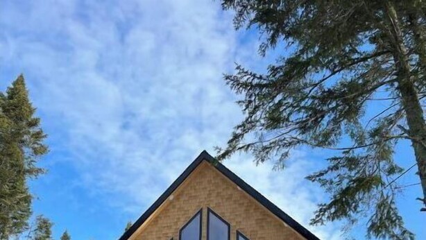 Een houten chalet met twee verdiepingen, grote ramen en een balkon.