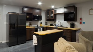 Eine moderne Küche mit dunklen Holzschränken, einem Edelstahlkühlschrank, einer Mikrowelle und einem Herd. Es gibt eine Holz Arbeitsplatte und ein Spülbecken mit einem Wasserhahn. Ein Handtuch hängt an einem schwarzen Schrankgriff.