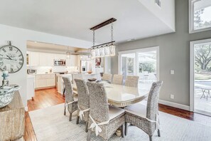 Una cocina moderna con armarios blancos, una isla central y un comedor con sillas de mimbre y una mesa de vidrio.