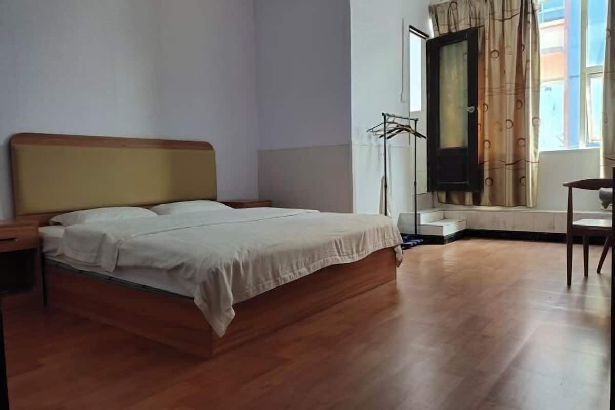 A bedroom with a wooden bed, a nightstand, a chair, a window with curtains, and a radiator.