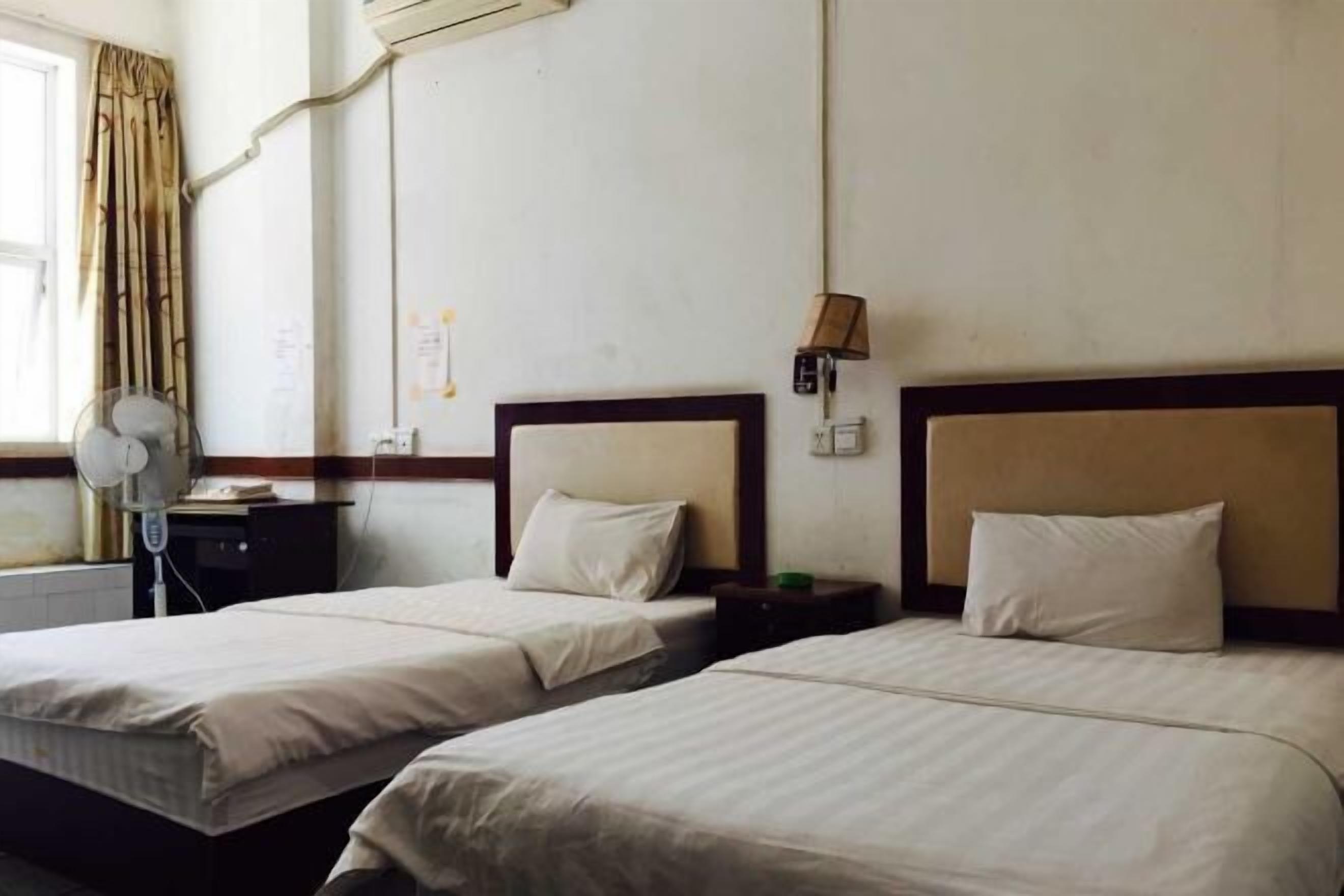 Habitación de hotel con dos camas, una mesita de noche, una lámpara y un equipo de aire acondicionado.