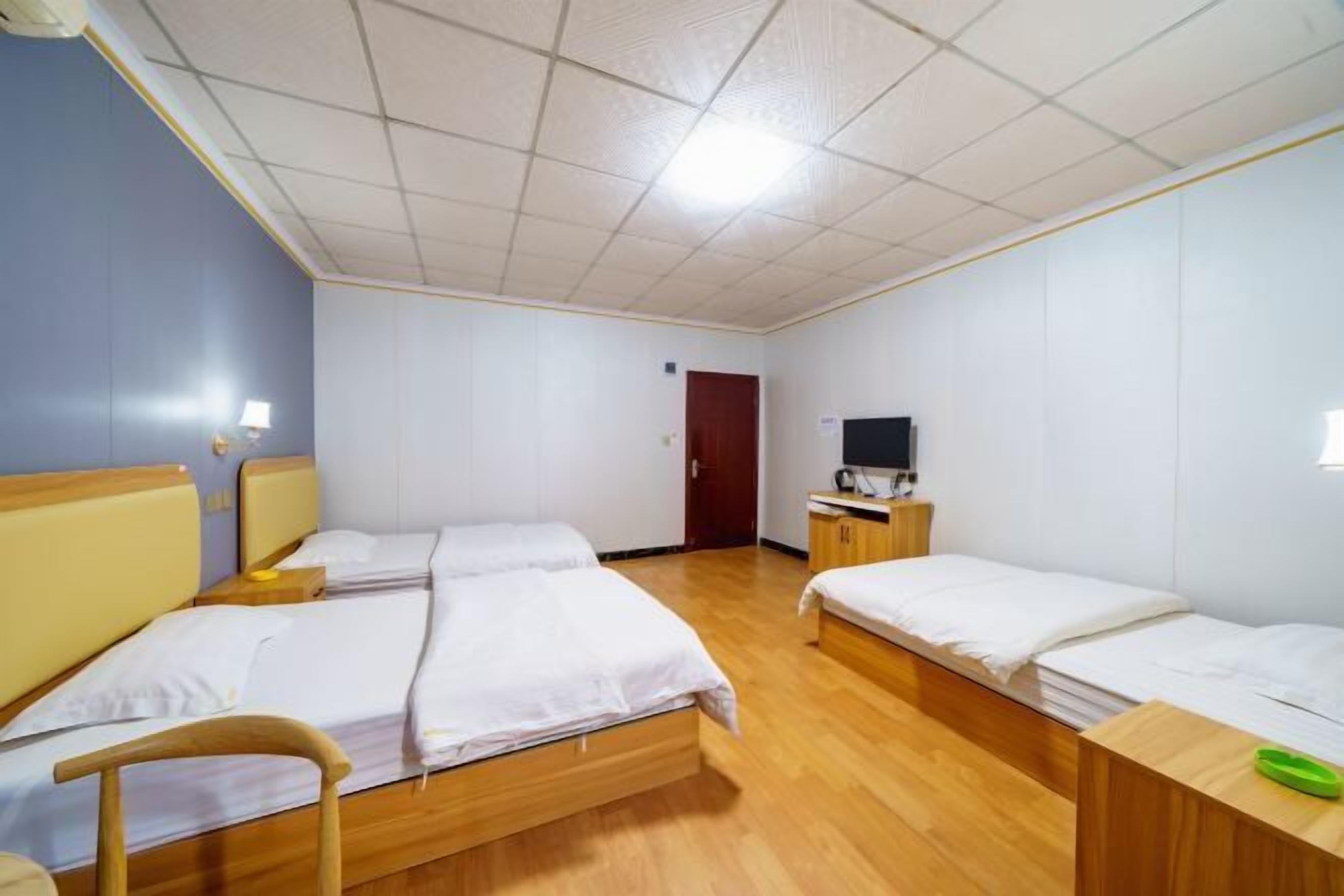 Habitación de hotel con dos camas individuales, piso de madera, televisor sobre un mueble de madera y una puerta al fondo.