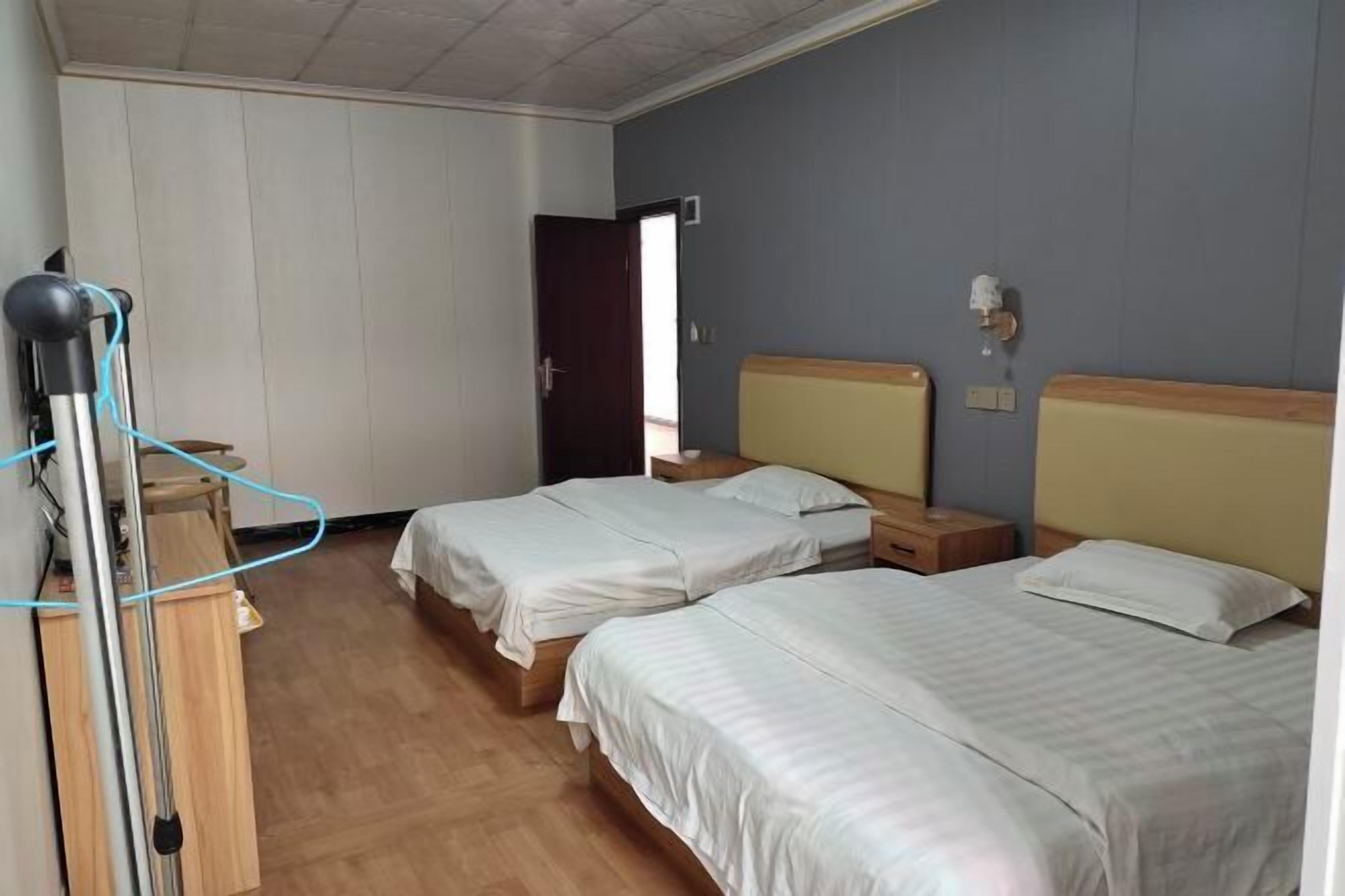Una habitación con dos camas, un escritorio de madera, una silla, un calentador portátil y una puerta.