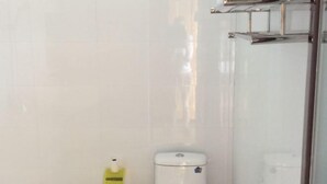 A bathroom with a white toilet, a yellow hand sanitizer dispenser, and a glass shower enclosure. - Qianxi Hotel (Deqin)