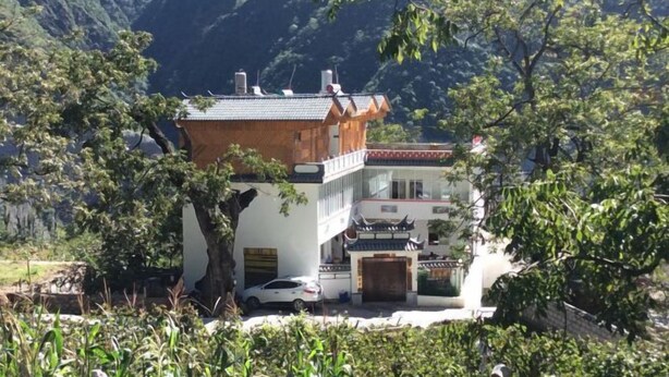 A traditional building with a sloped roof, surrounded by lush greenery and mountains in the background. - Qianxi Hotel (Deqin)